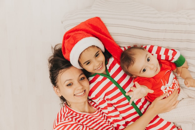 Family in striped pajamas resting at home. Little children are lying on the bed, wearing santa claus hats. A happy family.view from above