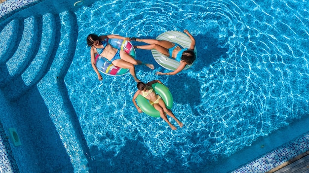 Family in swimming pool aerial drone view from above, happy mother and kids swim on inflatable ring donuts and have fun in water on family vacation, tropical holidays on resort