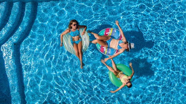 Семья в бассейне с высоты птичьего полета, счастливая мать и дети плавают на надувных кольцевых пончиках и веселятся в воде во время семейного отдыха, тропического отдыха на курорте