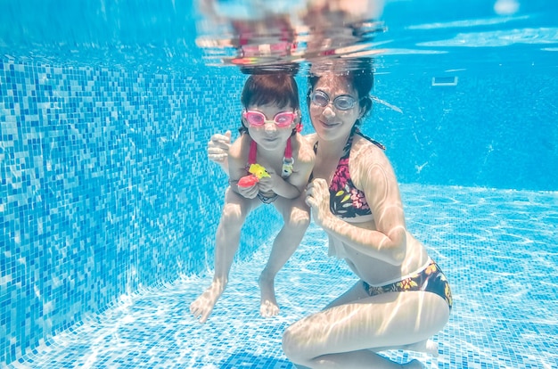 Family swims in pool underwater happy active mother and child have fun under water