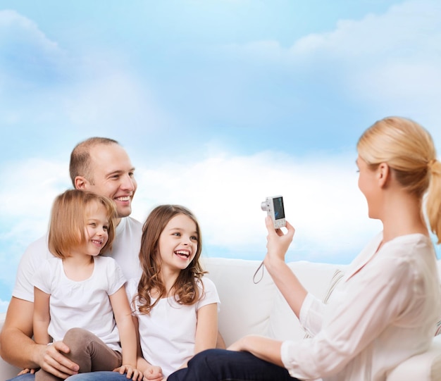 семья, технологии и люди - улыбающиеся мать, отец и маленькие девочки с камерой на фоне голубого неба