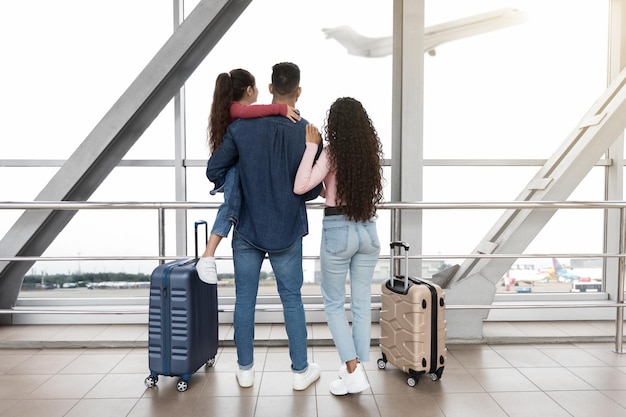 Family of three in airport looking out of window at airplane departure