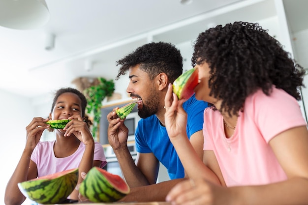 スイカを楽しんでいる3人の幸せな若い家族の家族スイカのスライスを食べて一緒に笑っている家族