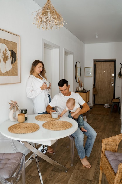 A family of three is having breakfast mom is standing drinking coffee dad and baby