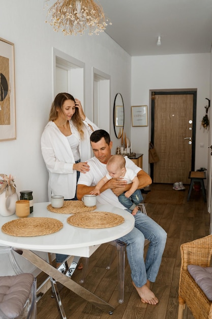 A family of three is having breakfast mom is standing drinking coffee dad and baby