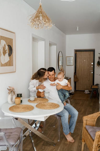 A family of three is having breakfast mom is standing drinking coffee dad and baby