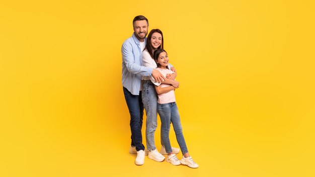 Family of three stands embracing each other against yellow background