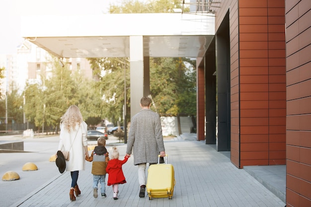 Foto famiglia di turisti, padre, madre, figlia e figlio con una valigia gialla entrano in albergo.