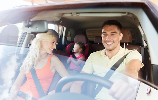 family, transport, safety, road trip and people concept - happy man and woman with little child driving in car