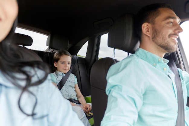 family, transport, safety, road trip and people concept - happy man and woman with little child driving in car