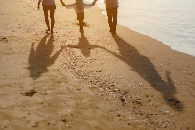 Family, travel, beach, relax, lifestyle, holiday concept. Family who enjoy a picnic. Parents are holding hands their children and walking on the beach at sunset in holiday.