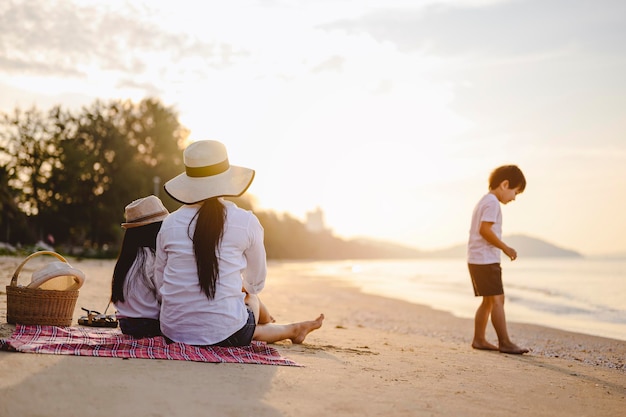 家族、旅行、ビーチ、リラックス、ライフスタイル、休日のコンセプト。休日の日没時にビーチでピクニックを楽しむ親子。