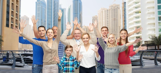 family, travel, tourism and people concept - group of smiling men, women and boy having fun and waving hands over dubai city street background