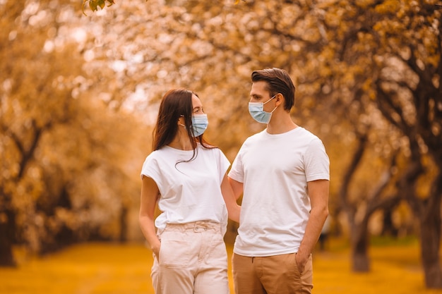 秋の屋外でウイルスを防ぐための保護医療マスクを身に着けている2人家族