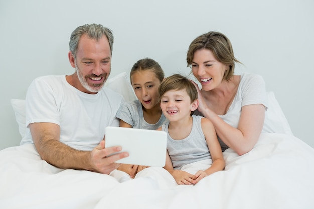 Family using digital tablet on bed in bedroom at home