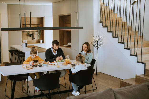 Family using mobile phones while having breakfast at dining table at the apartment