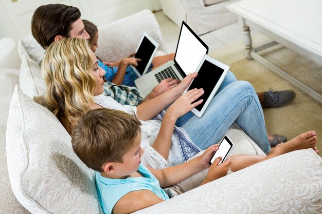 Foto famiglia che utilizza varie tecnologie, seduti sul divano