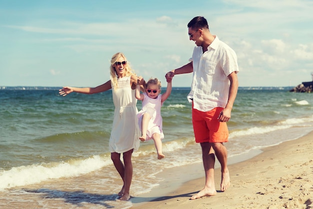 Foto concetto di famiglia, vacanza, adozione e persone - uomo felice, donna e bambina in occhiali da sole che camminano e si divertono sulla spiaggia estiva