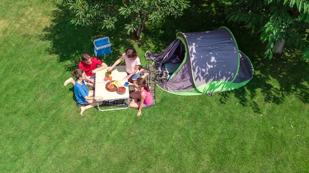 Family vacation in campsite aerial top view from above, parents and kids relax and have fun in park, tent and camping equipment under tree, family in camp outdoors concept