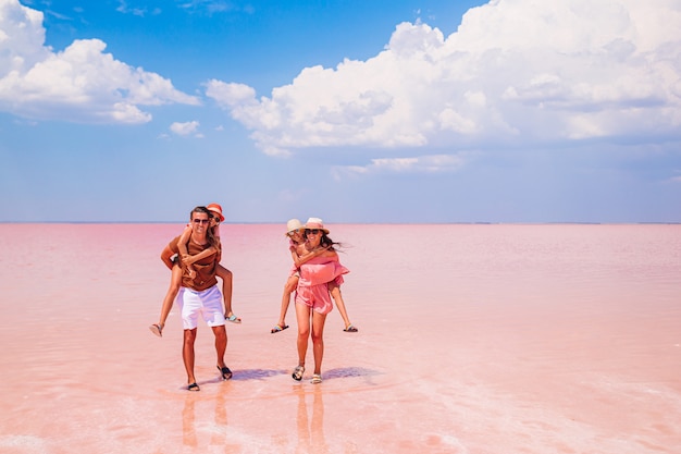Семейный отдых. счастливые родители с двумя детьми на розовое соленое озеро в солнечный летний день. изучение природы, путешествий, семейного отдыха.