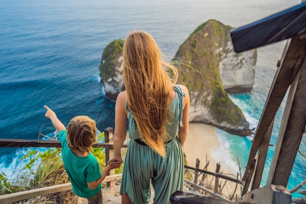 Family vacation lifestyle Happy mother and son stand at viewpoint Look at beautiful beach under high cliff Travel destination in Bali Popular place to visit on Nusa Penida island