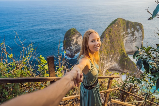Family vacation lifestyle Happy woman stand at viewpoint Look at beautiful beach under high cliff Travel destination in Bali Popular place to visit on Nusa Penida island