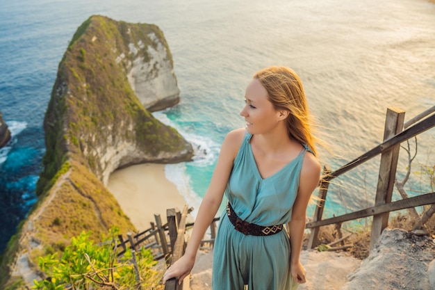 Family vacation lifestyle Happy woman stand at viewpoint Look at beautiful beach under high cliff Travel destination in Bali Popular place to visit on Nusa Penida island