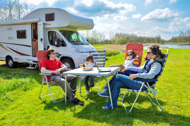 家族での休暇、RV（キャンピングカー）は子供と一緒に旅行、子供と幸せな親はキャンピングカーでの休日の旅行でキャンプのテーブルに座る