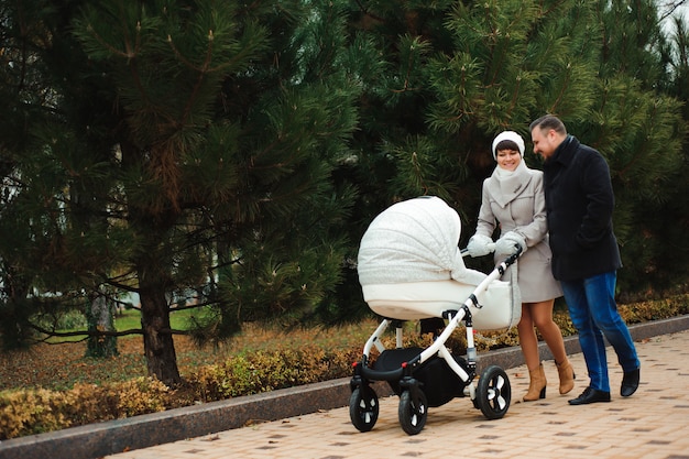 Family walk in the autumn park with a pram. Mom, dad and baby