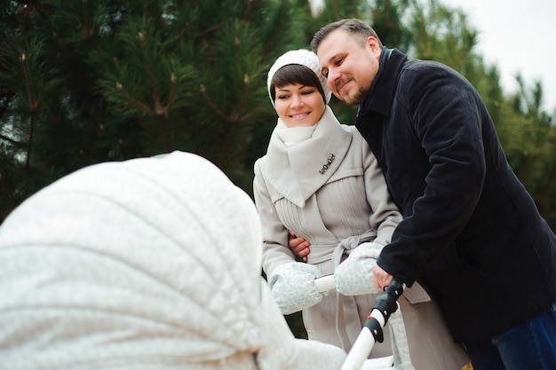 Foto famiglia a piedi nel parco in autunno con una carrozzina. mamma, papà e bambino