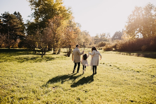 Family walking in a park Father mother and daughter having fun holding hands on a warm spring day