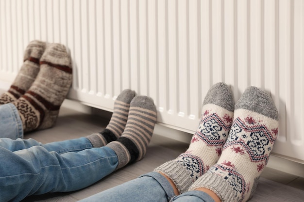 Family warming legs near heating radiator indoors closeup