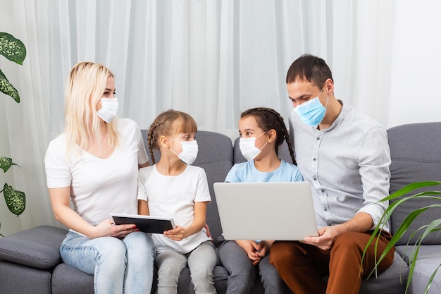 Family waving and greeting someone during video call at home. Parents are wearing protective face masks.