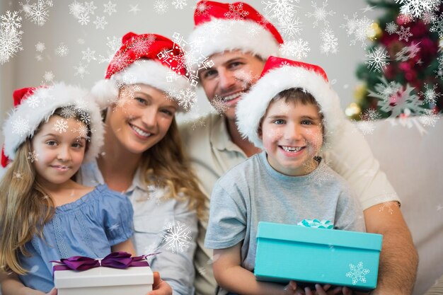 Family wearing christmas hat while holding presents against snowflakes