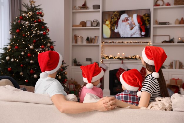 Family wearing Christmas hats watching TV in cosy room back view Winter holidays atmosphere