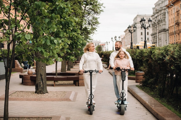 Семья в белых одеждах катается на электросамокатах по городу.