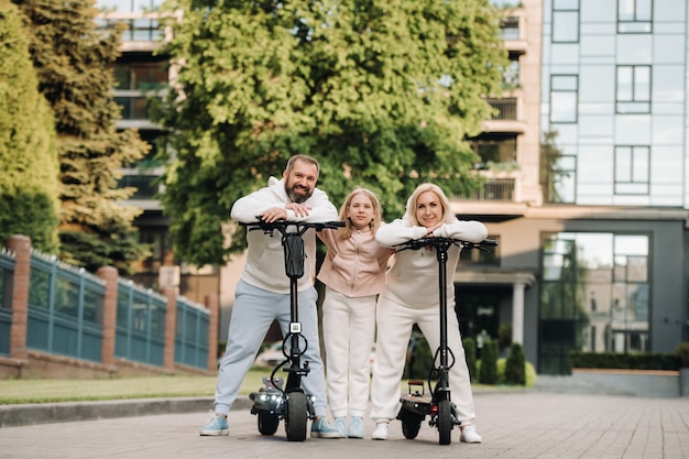 A family in white clothes stands in the city on electric scooters.