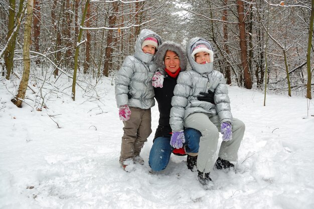Семья в зимнем лесу, счастливая мать и дети веселятся на свежем воздухе
