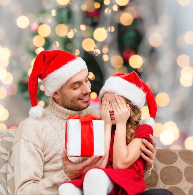 family, winter holidays and people concept - smiling daughter with closed eyes waiting for present from father over living room and christmas tree background