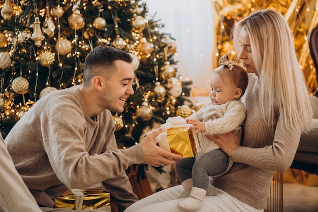 Family with baby daughter holding Christmas gift under the tree