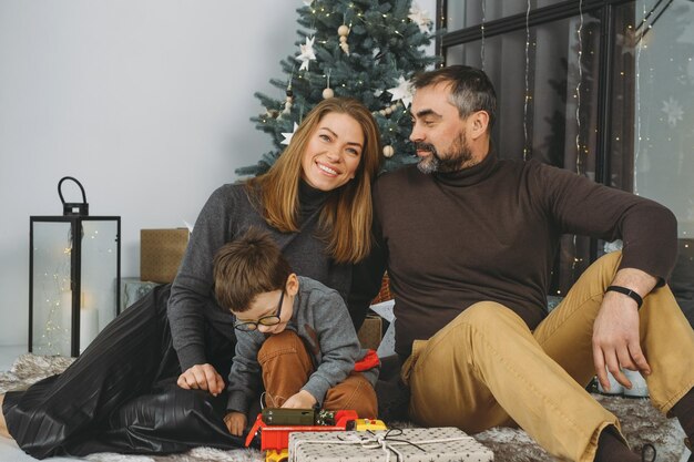 Family with child playing near christmas tree child unpacking gifts parents enjoy christmas tree