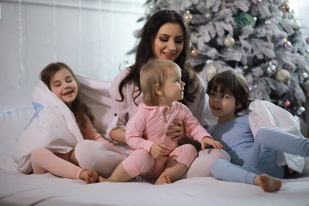 Семья с детьми веселится на кровати под одеялом во время рождественских каникул.