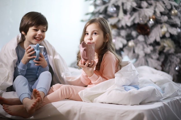 クリスマス休暇中にカバーの下のベッドで楽しんでいる子供を持つ家族。