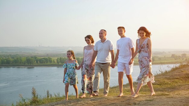 Family with children walks joining hands along riverbank