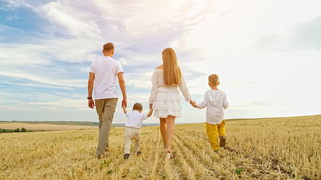 Family with children walks joining hands on mown wheat field