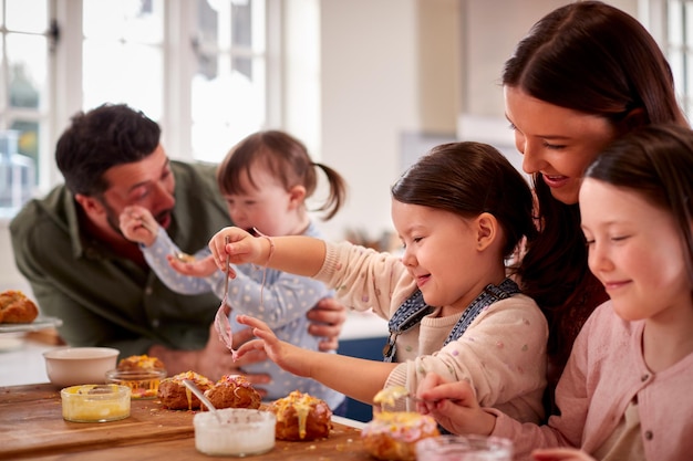 Family With Down Syndrome Daughter Baking And Decorating Cakes Sitting Around Table At Home