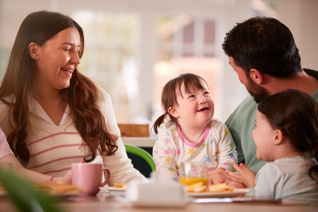 Famiglia con la figlia di sindrome di down che si siede intorno al tavolo a casa che mangia la colazione