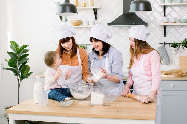 Family with grandmother, two daughters and little baby girl baking at kitchen. Grandmother adds sugar to the dough. Mother's Day concept, family baking