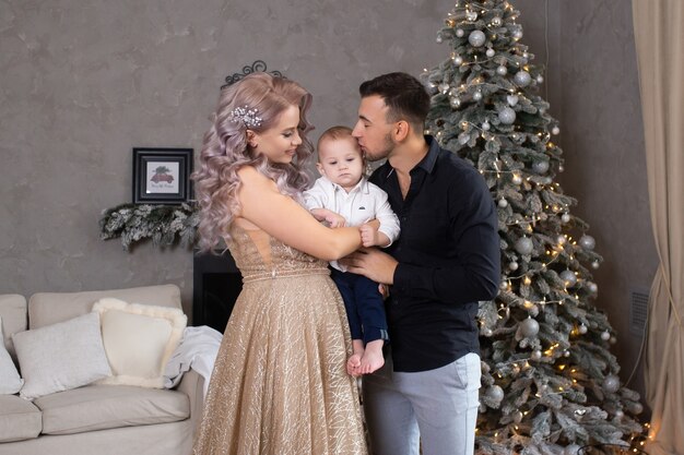 Family with little baby boy enjoying their time together at home near Christmas tree