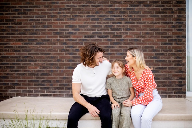 Family with a mother father and daughter sitting outside on the steps of a front porch of a brick house